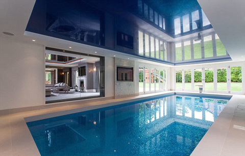 Bể bơi trong nhà được bao bọc bởi các tấm kính, nhìn ra được phòng khách và khu vườn