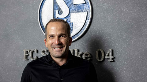 Manuel Baum đứng trước bức tường có logo của Schalke trong buổi lễ nhận chức HLV trưởng đội bóng này