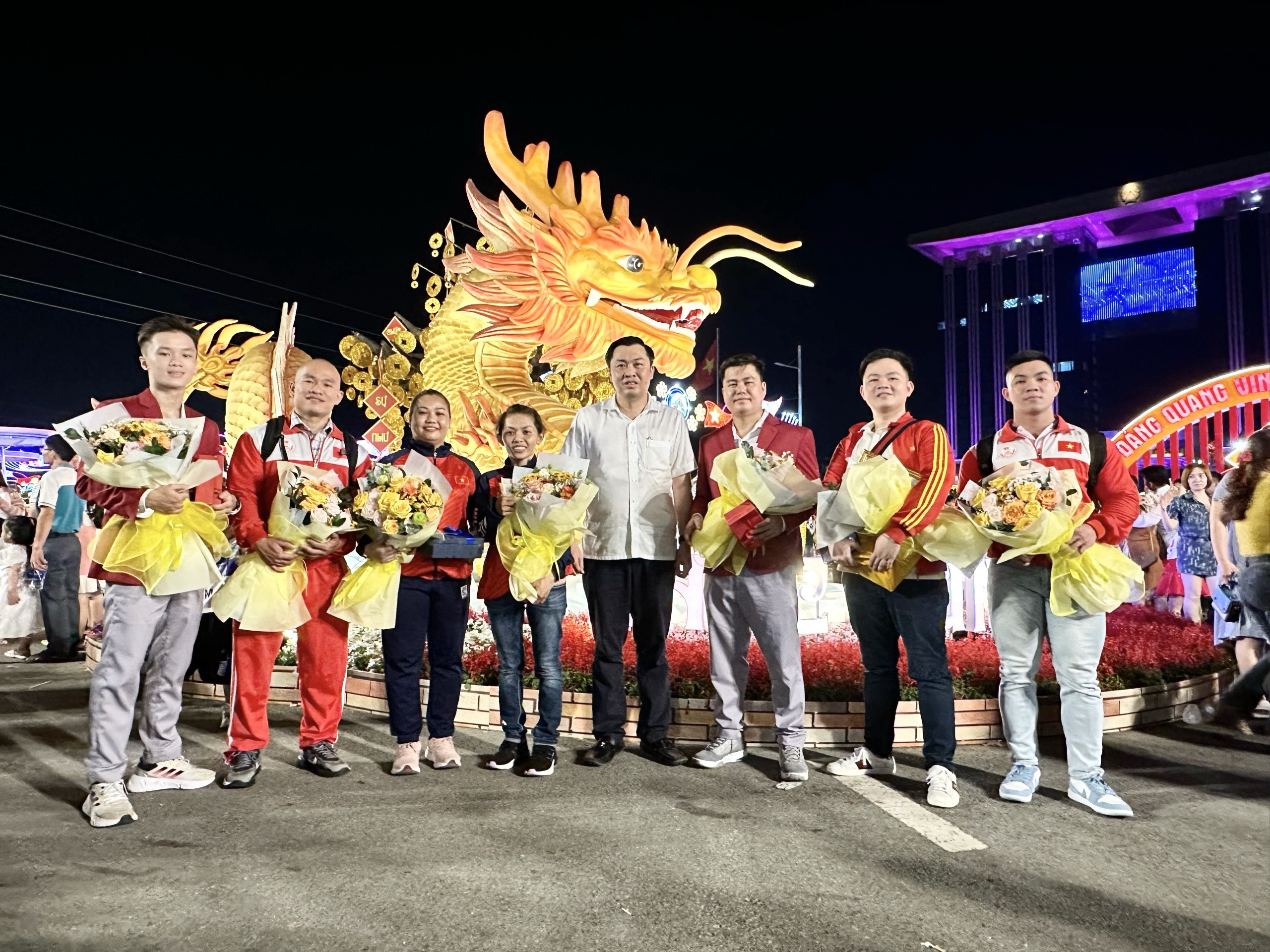 Ông Cao Văn Chóng – Phó Giám đốc Sở Văn hoá Thể thao và Du lịch tỉnh Bình Dương chụp hình lưu niệm cùng các vận động viên được tuyên dương công dân tiêu biểu trước linh vật rồng vàng có thể cử động tại khu vực Hội hoa Xuân Bình Dương, nơi diễn ra lễ tuyên dương